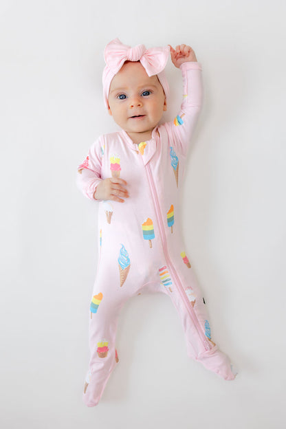 Baby wearing Zippered footie in Sakura Ice cream print with pink bow headband on a white background