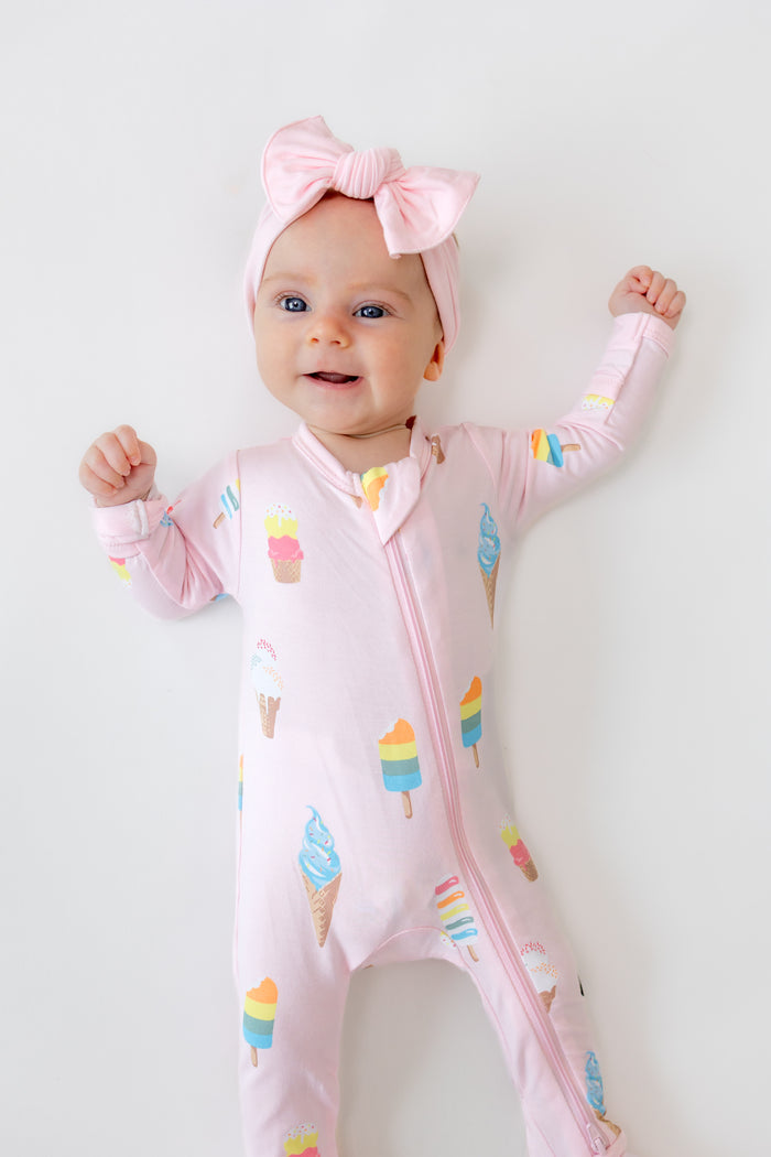 Baby in Sakura Ice cream print zippered footie with pink bow headband on a white background