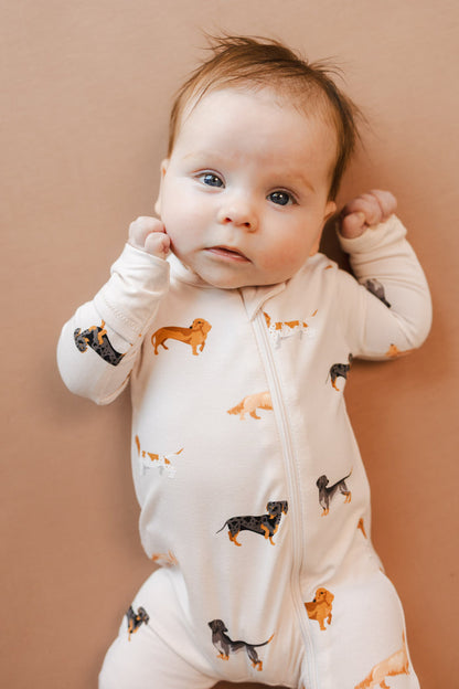 Baby wearing Beige Zippered Romper in Dachshund print on a brown background