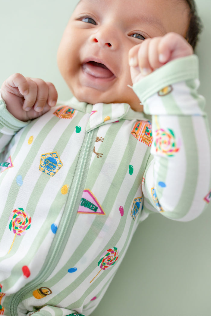 Smiling baby in a green and white striped zippered romper with colorful Harry Potter patterns on a green background