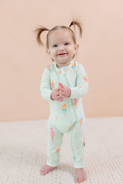 Child wearing a light green zippered onesie with colorful ice cream patterns on a beige background