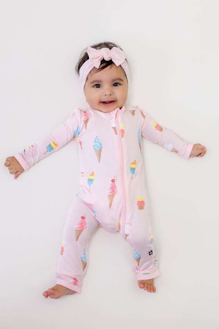 Baby wearing Zippered romper in Sakura Ice cream print with pink bow headband on a white background