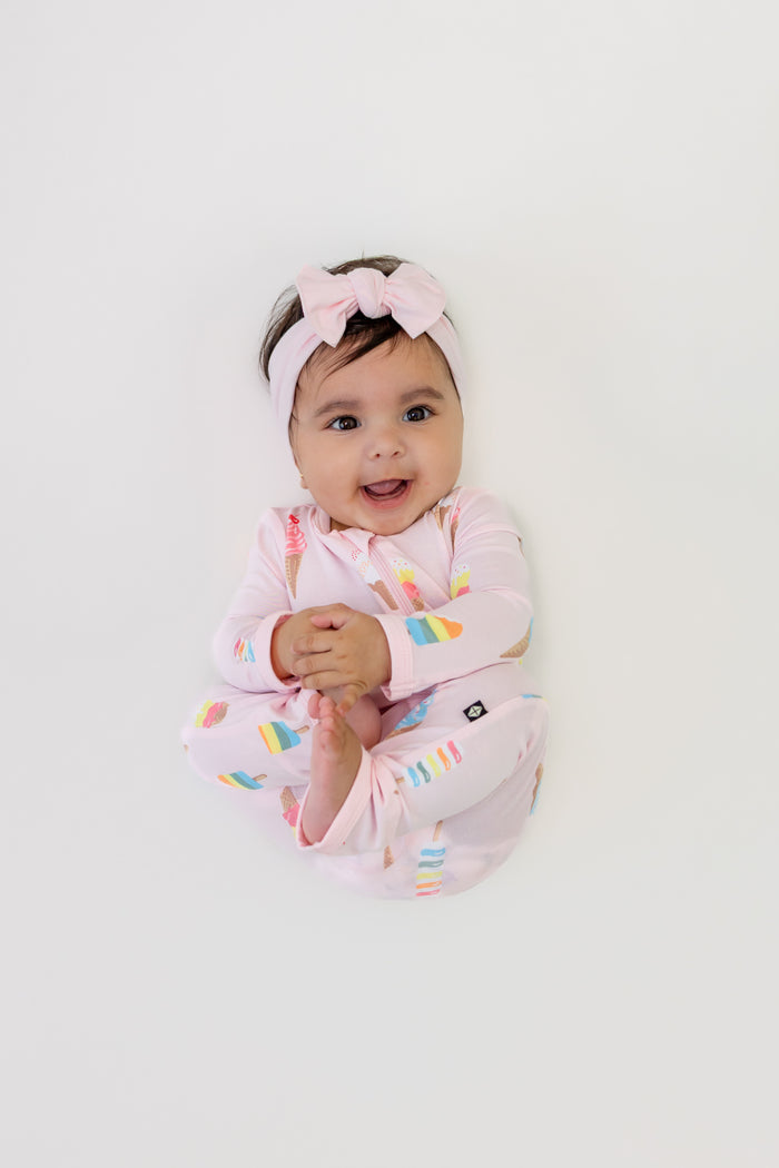 Baby wearing Sakura Ice cream print Zippered romper with pink bow headband on a white background